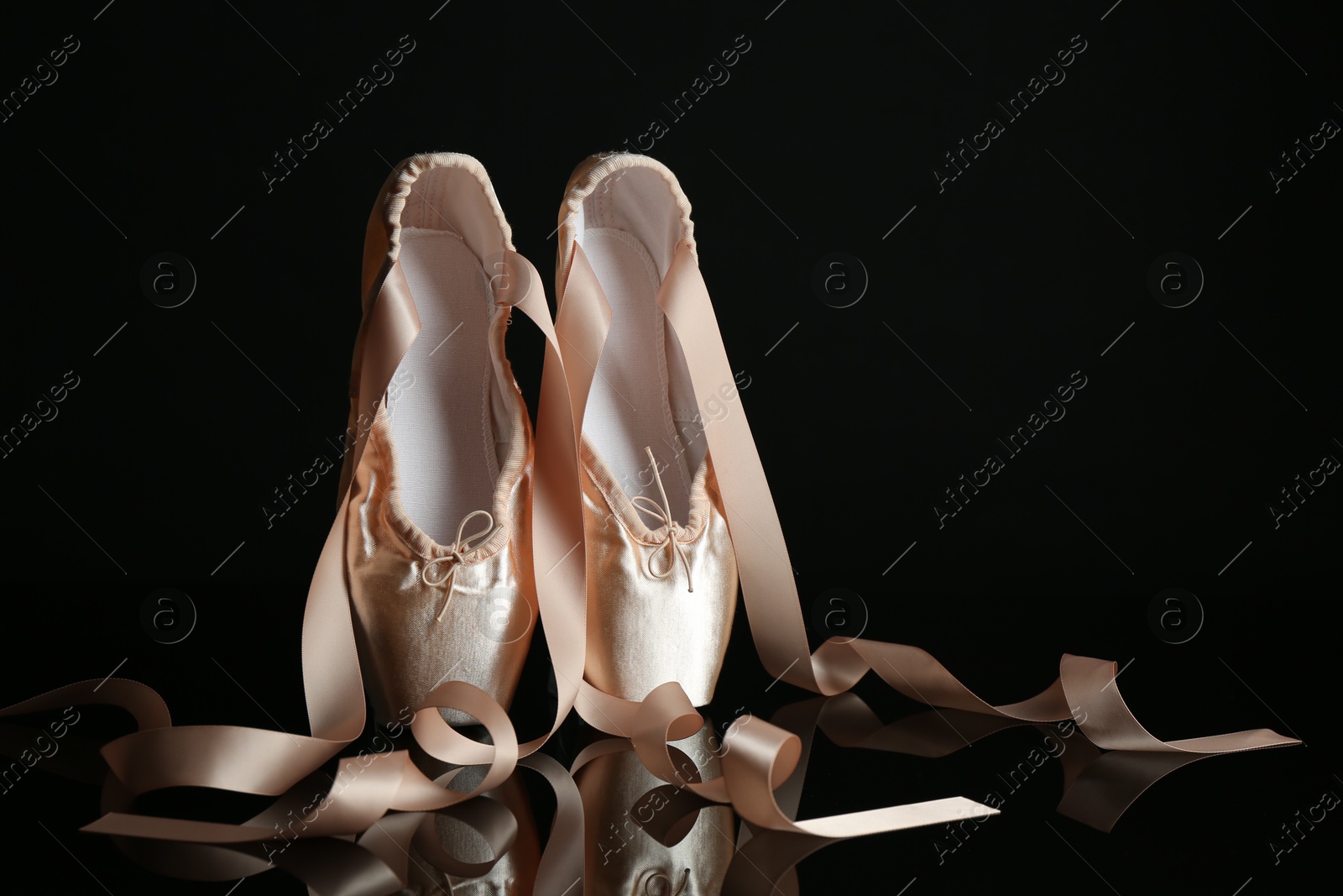 Photo of Pair of beautiful pointe shoes on black mirror surface, space for text