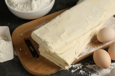 Photo of Raw puff pastry dough, eggs and flour on dark table, closeup