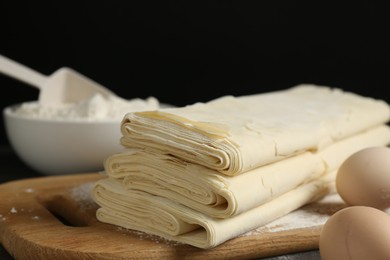 Photo of Board with raw puff pastry dough, eggs and flour on table, closeup