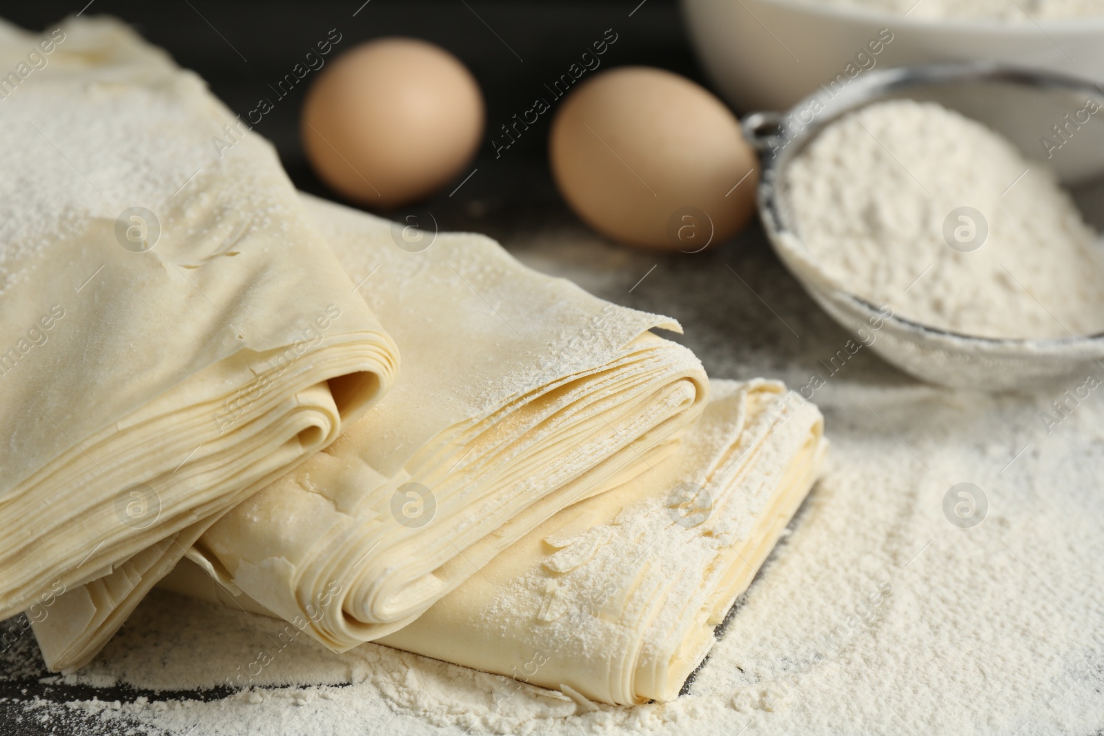 Photo of Raw puff pastry dough, eggs and flour on table, closeup