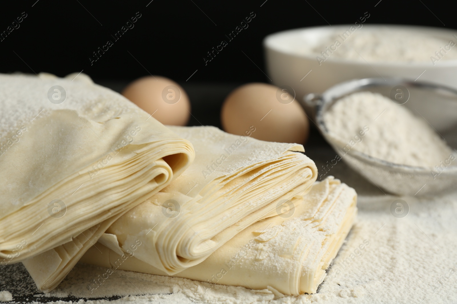 Photo of Raw puff pastry dough, eggs and flour on table, closeup