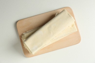 Photo of Board with raw puff pastry dough on white table, top view