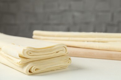 Photo of Stack of raw puff pastry dough on white table, closeup. Space for text