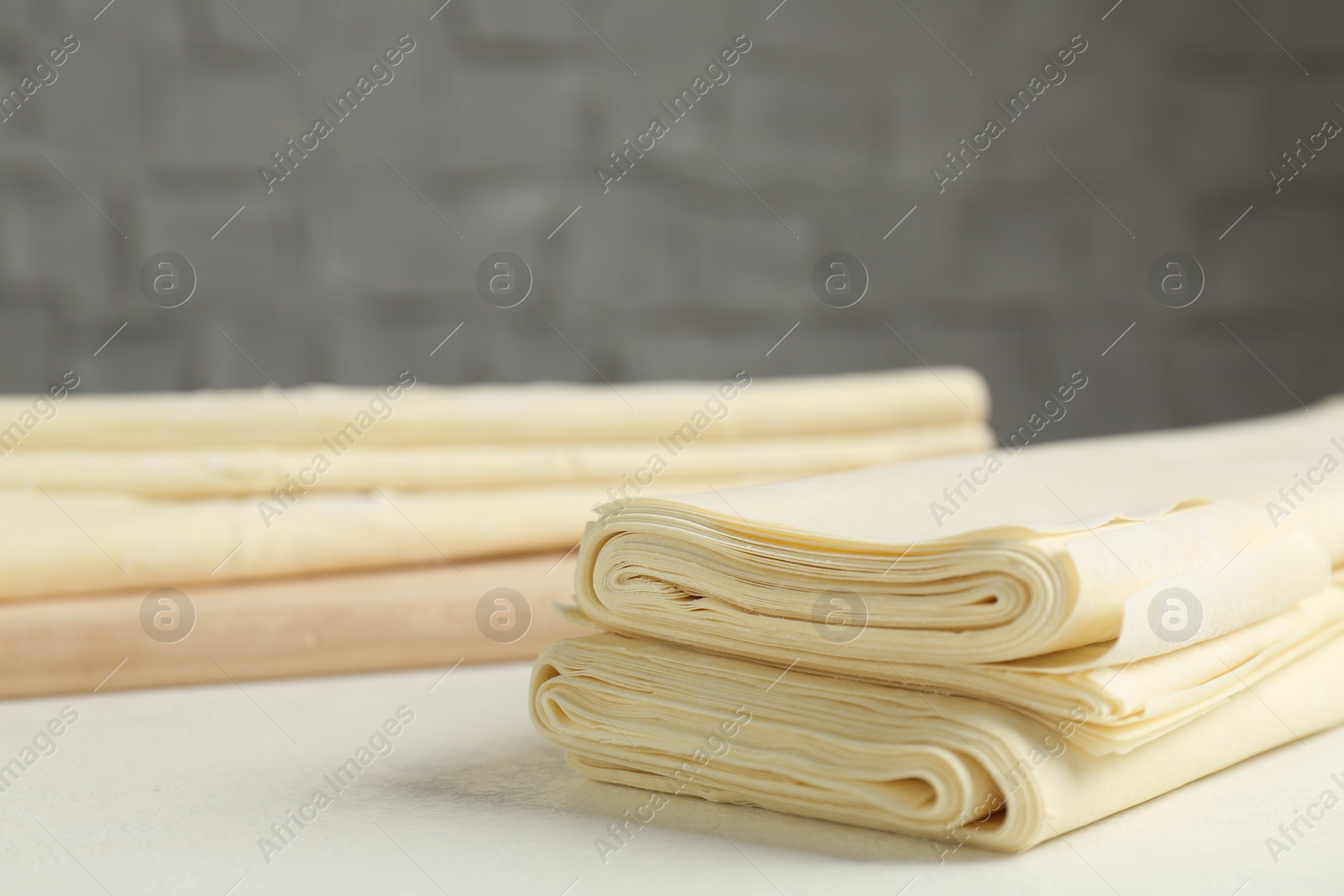 Photo of Stack of raw puff pastry dough on white table, closeup. Space for text