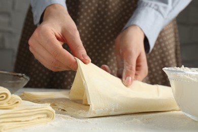 Photo of Woman making puff pastry dough at white table, closeup