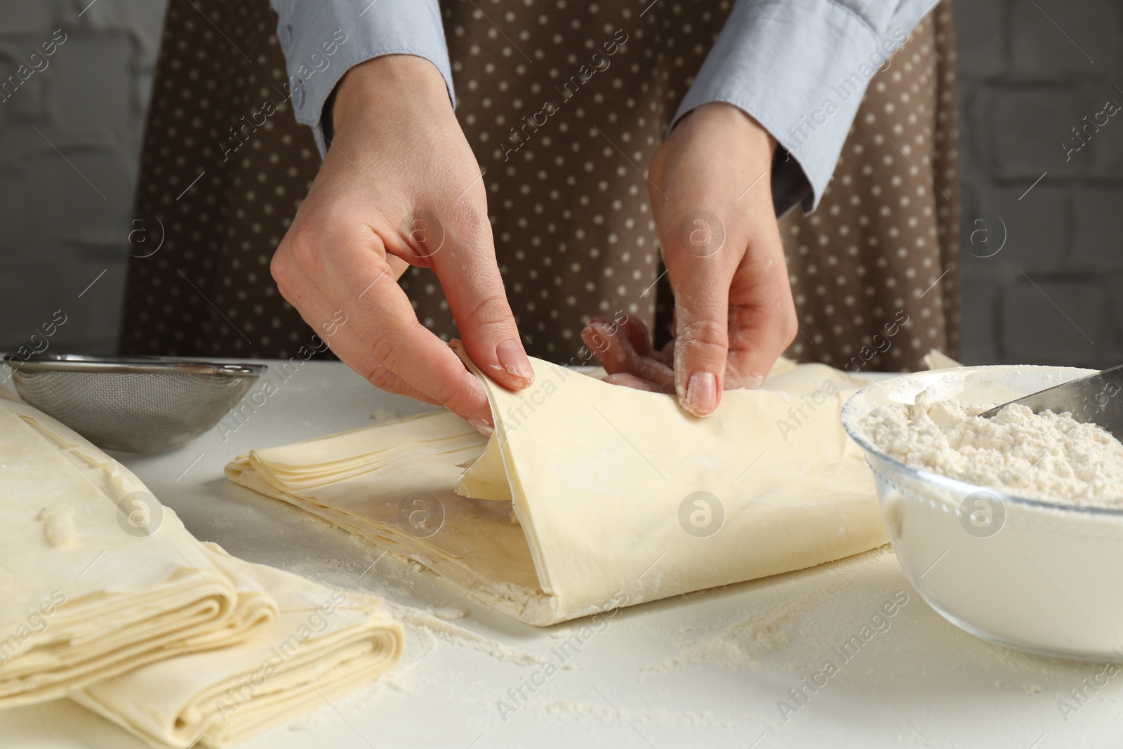 Photo of Woman making puff pastry dough at white table, closeup