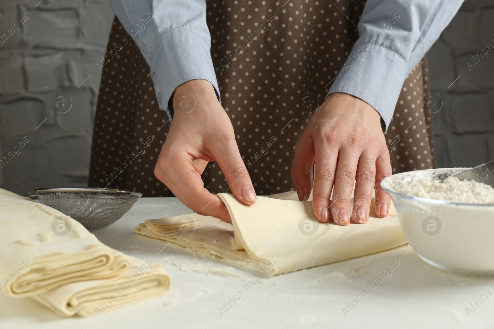 Photo of Woman making puff pastry dough at white table, closeup