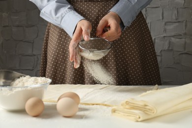 Photo of Woman making puff pastry dough at white table, closeup