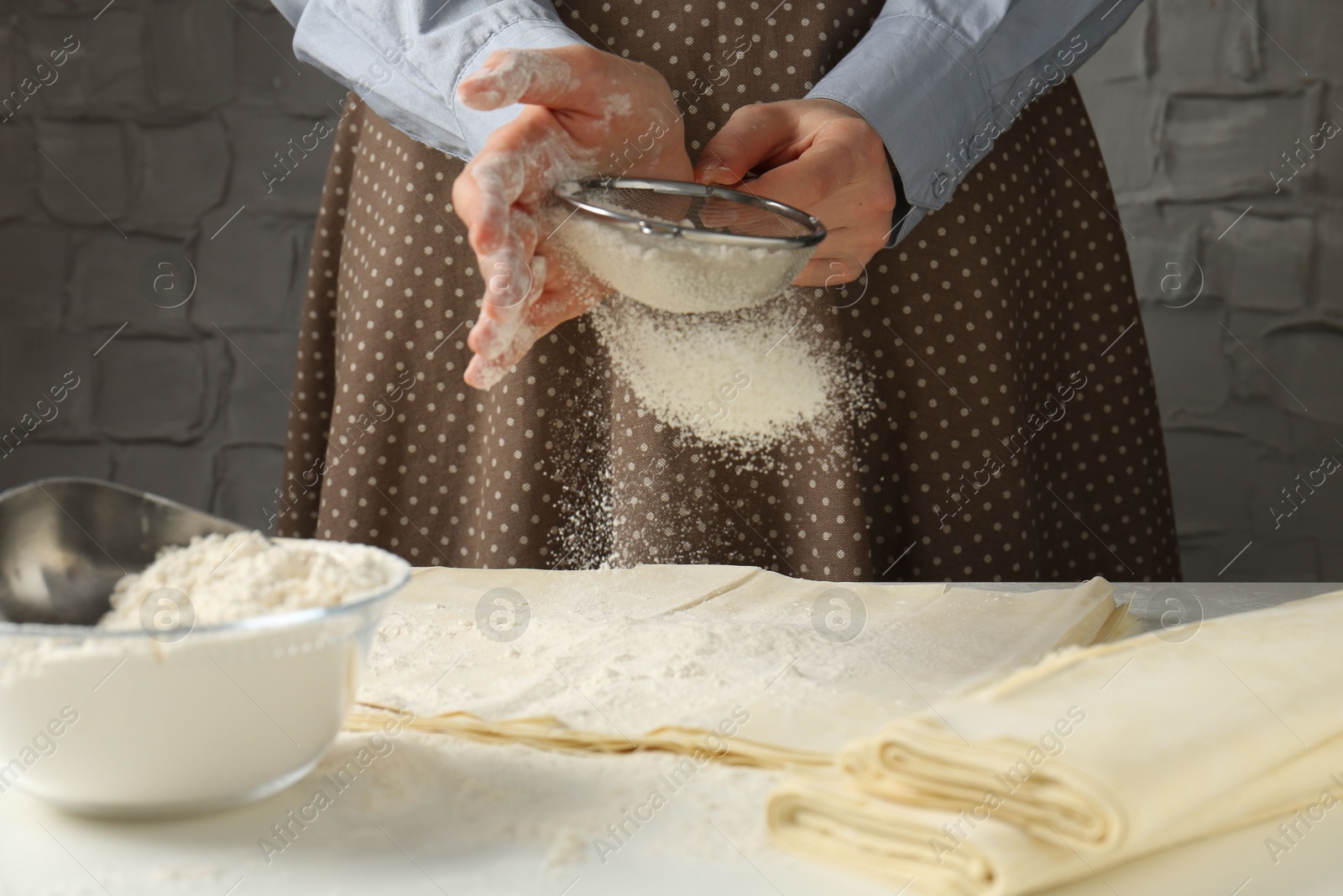 Photo of Woman making puff pastry dough at white table, closeup