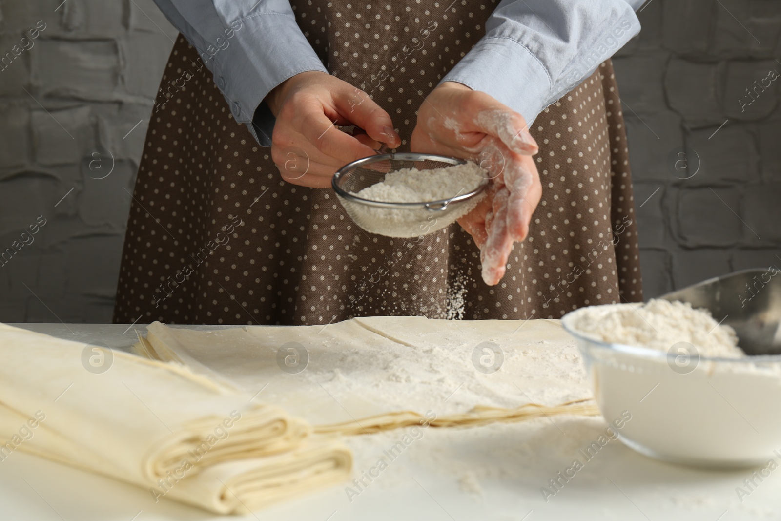 Photo of Woman making puff pastry dough at white table, closeup