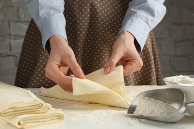 Photo of Woman with puff pastry dough at white table, closeup