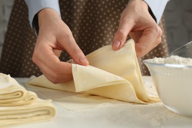 Photo of Woman with puff pastry dough at white table, closeup