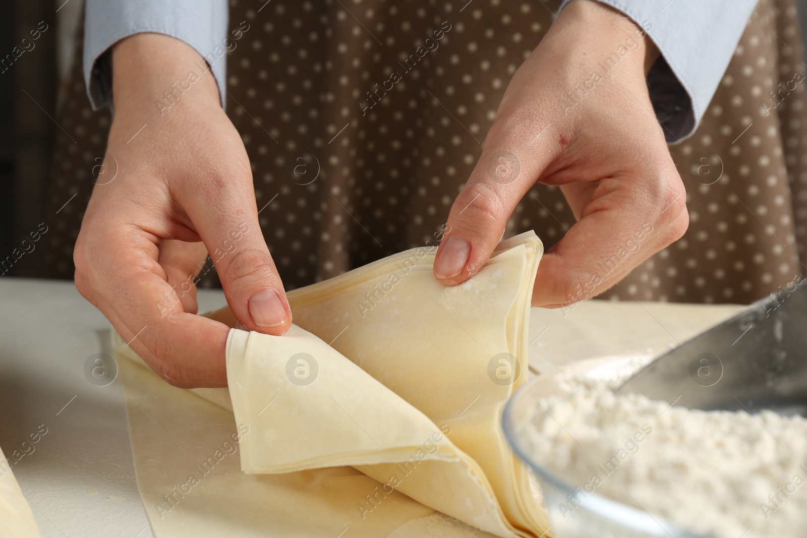 Photo of Woman with puff pastry dough at white table, closeup