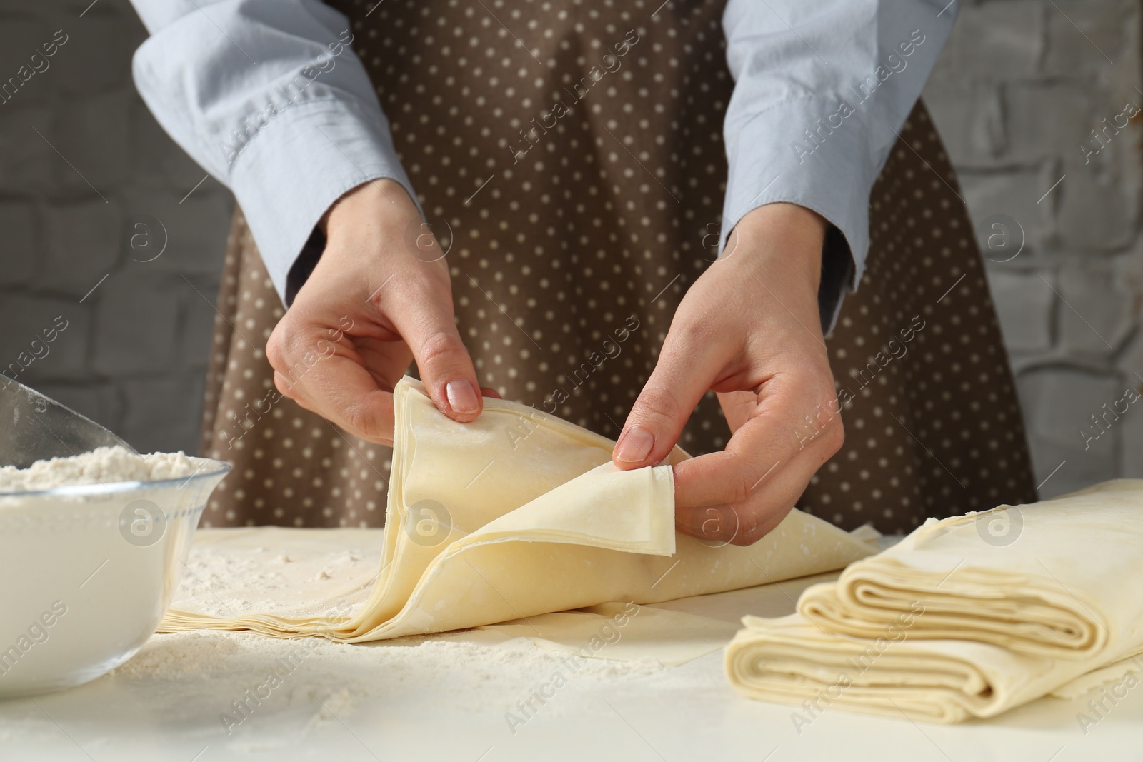 Photo of Woman with puff pastry dough at white table, closeup