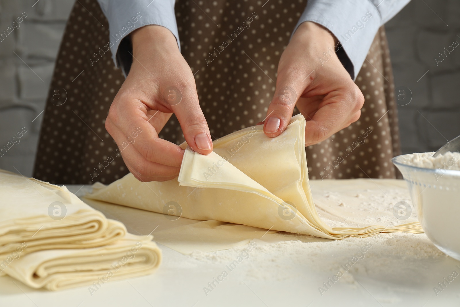 Photo of Woman with puff pastry dough at white table, closeup