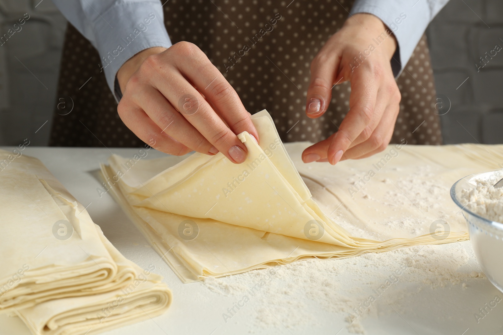 Photo of Woman with puff pastry dough at white table, closeup