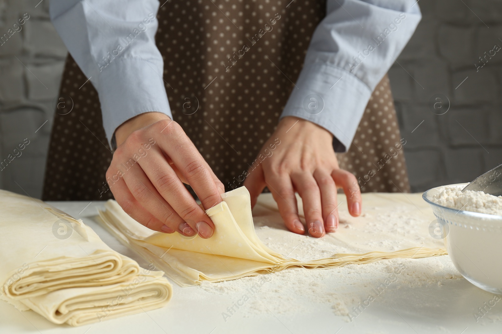 Photo of Woman with puff pastry dough at white table, closeup