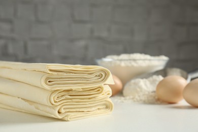 Photo of Stack of raw puff pastry dough on white table, closeup. Space for text