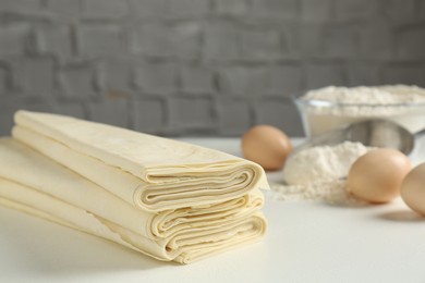 Photo of Stack of raw puff pastry dough on white table, closeup. Space for text