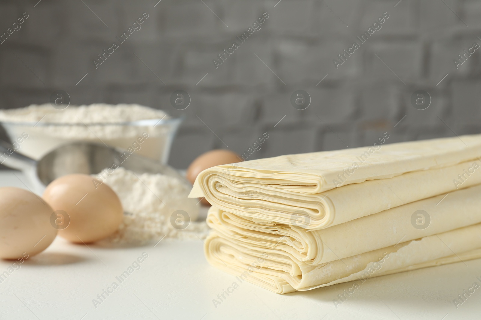 Photo of Stack of raw puff pastry dough on white table, closeup. Space for text