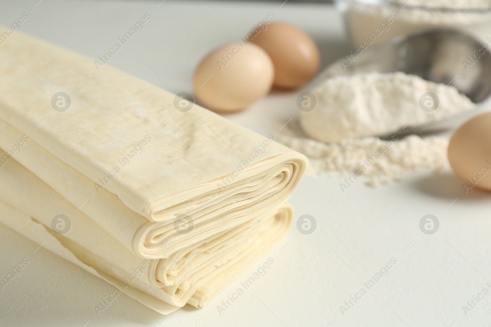 Photo of Stack of raw puff pastry dough on white table, closeup. Space for text