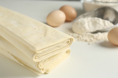 Photo of Stack of raw puff pastry dough on white table, closeup. Space for text