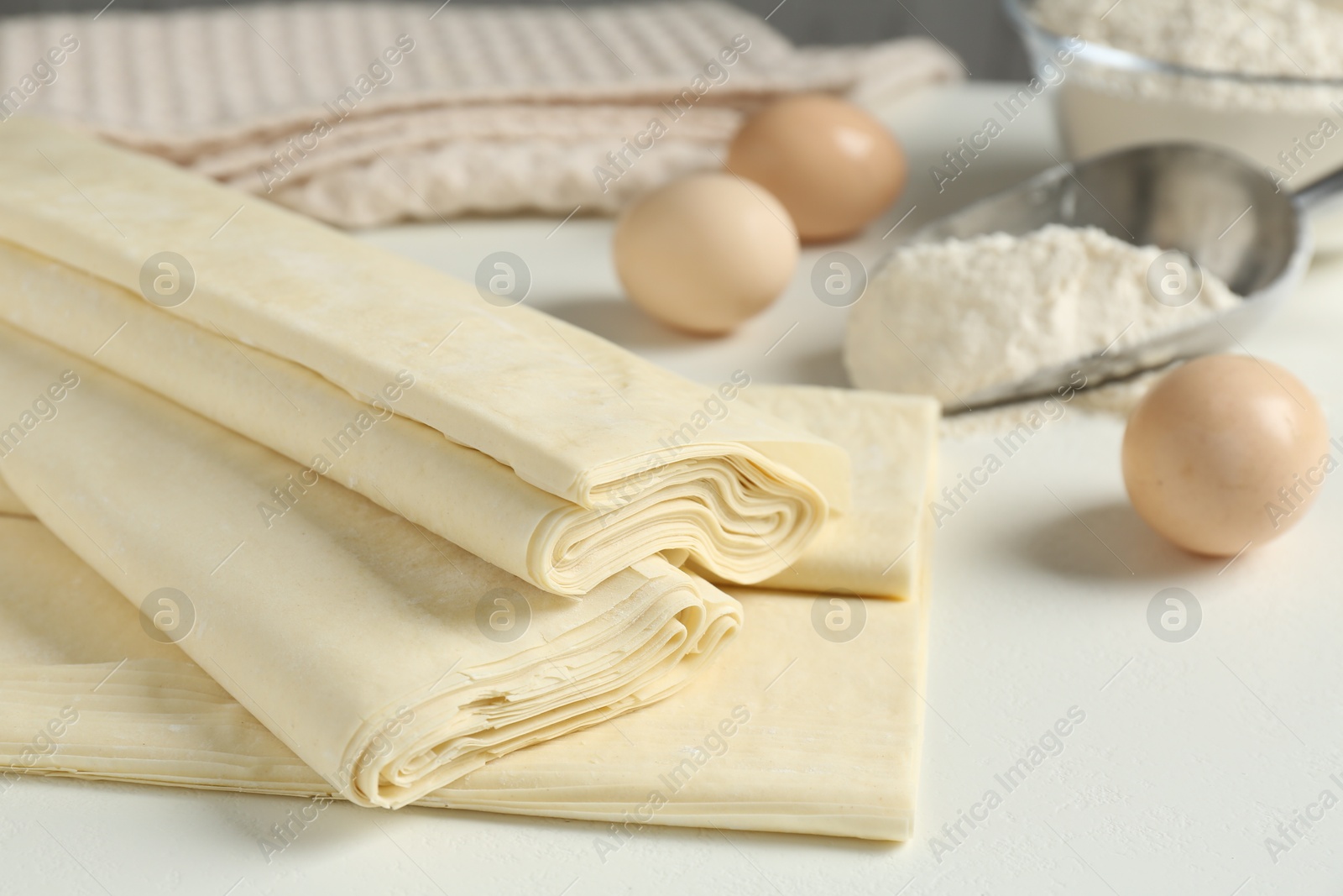 Photo of Raw puff pastry dough on white table, closeup