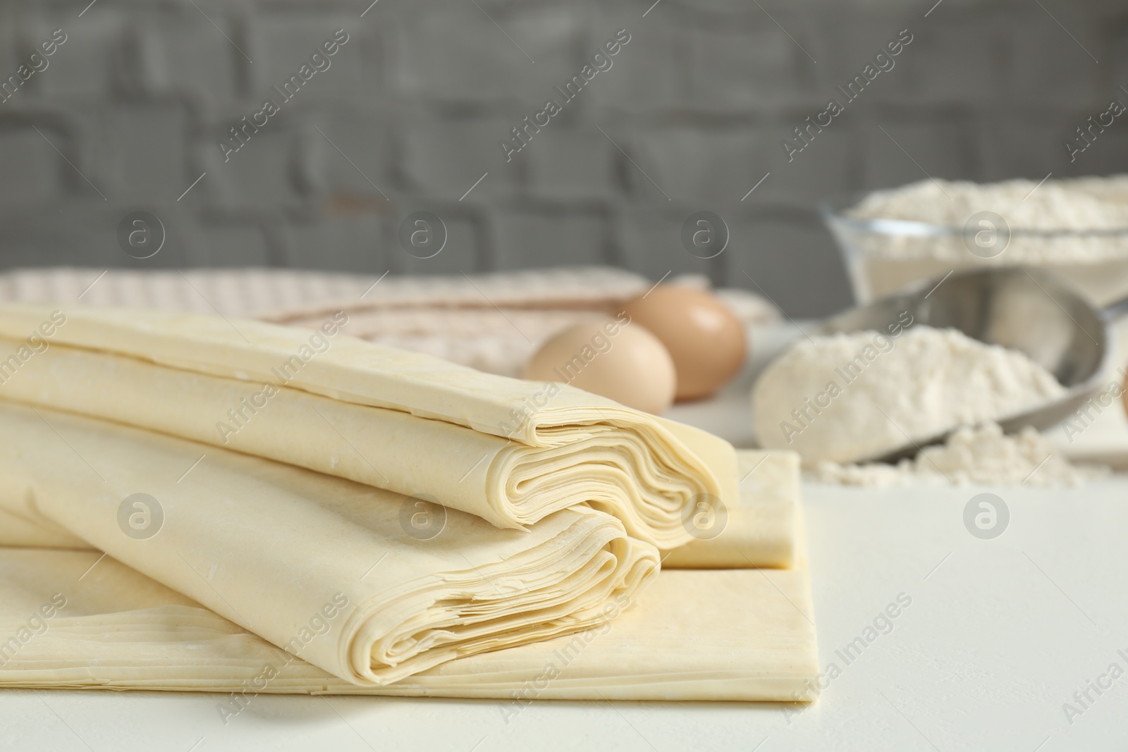 Photo of Raw puff pastry dough on white table, closeup. Space for text