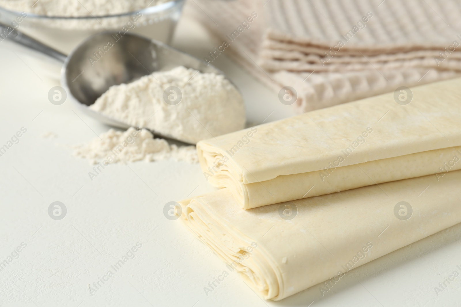 Photo of Raw puff pastry dough on white table, closeup. Space for text