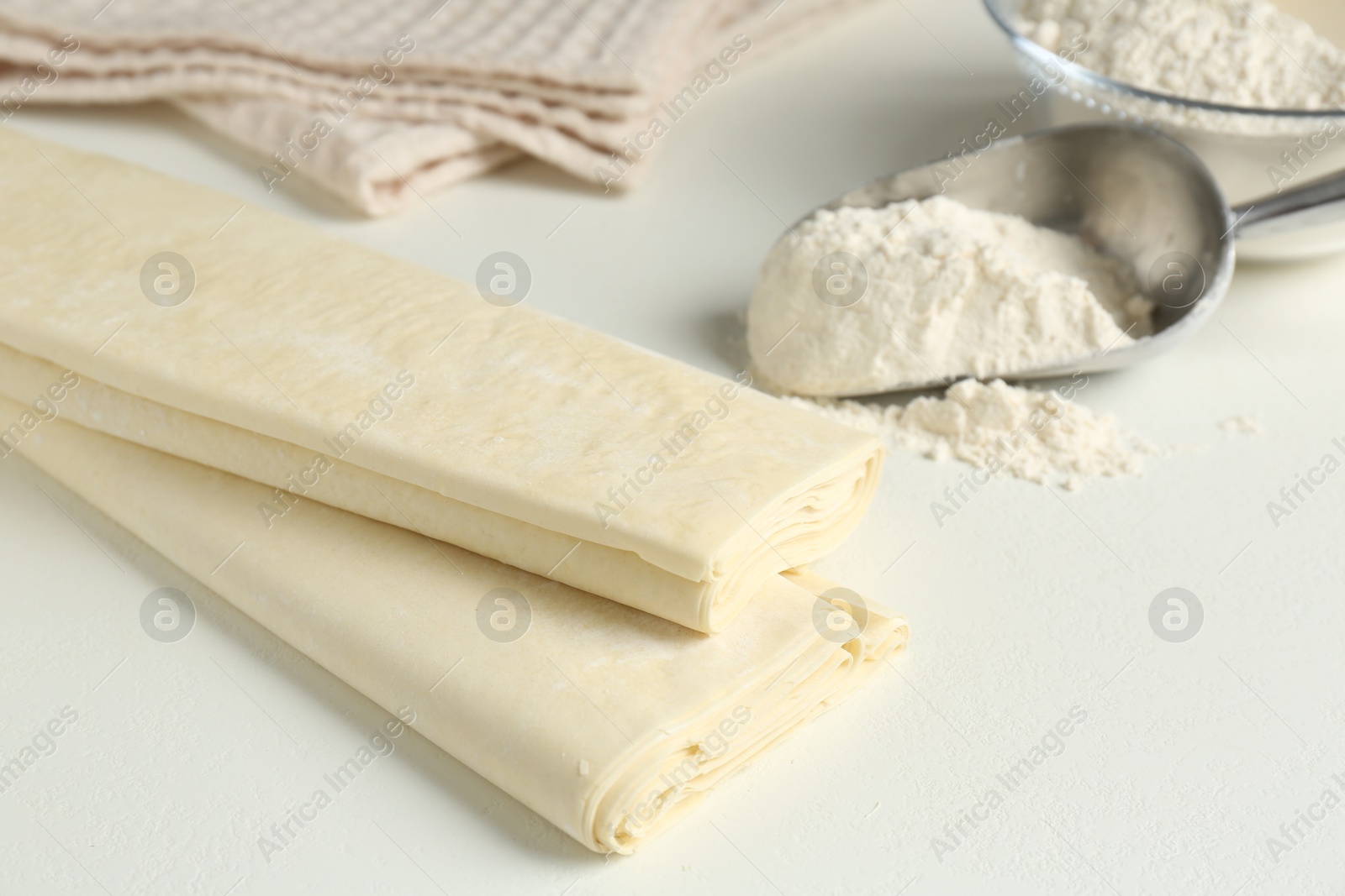 Photo of Raw puff pastry dough and flour on white table