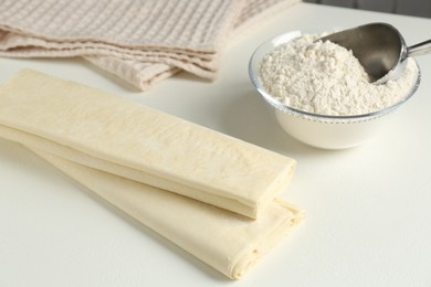 Photo of Raw puff pastry dough and flour on white table