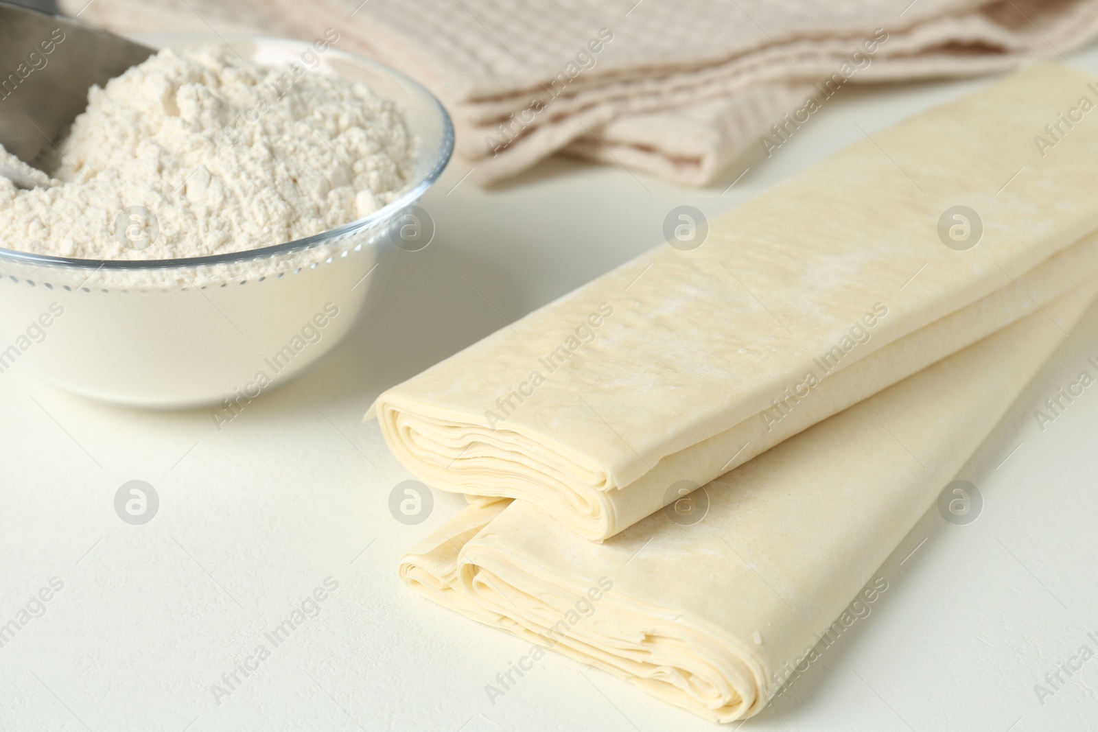 Photo of Raw puff pastry dough and flour on white table, closeup