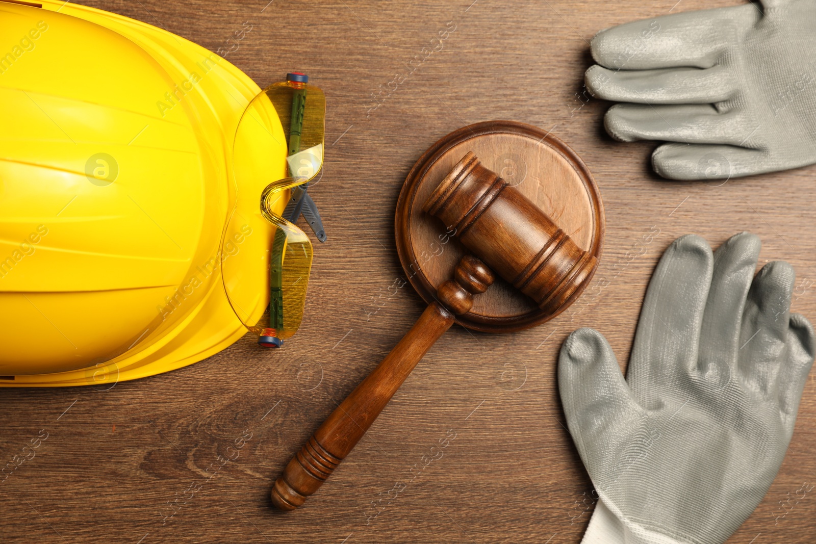 Photo of Accident at work concept. Gavel and protective gear on wooden table, flat lay