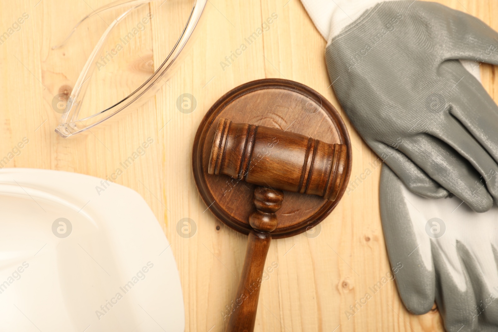 Photo of Accident at work concept. Gavel and protective gear on wooden table, flat lay