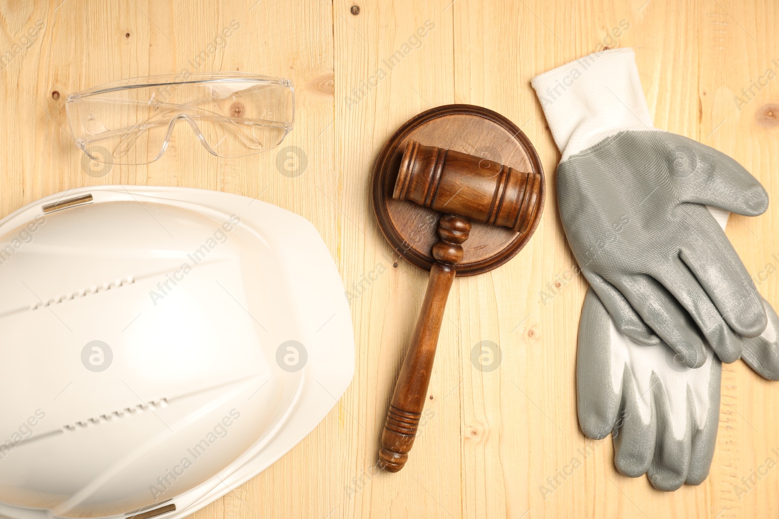 Photo of Accident at work concept. Gavel and protective gear on wooden table, flat lay