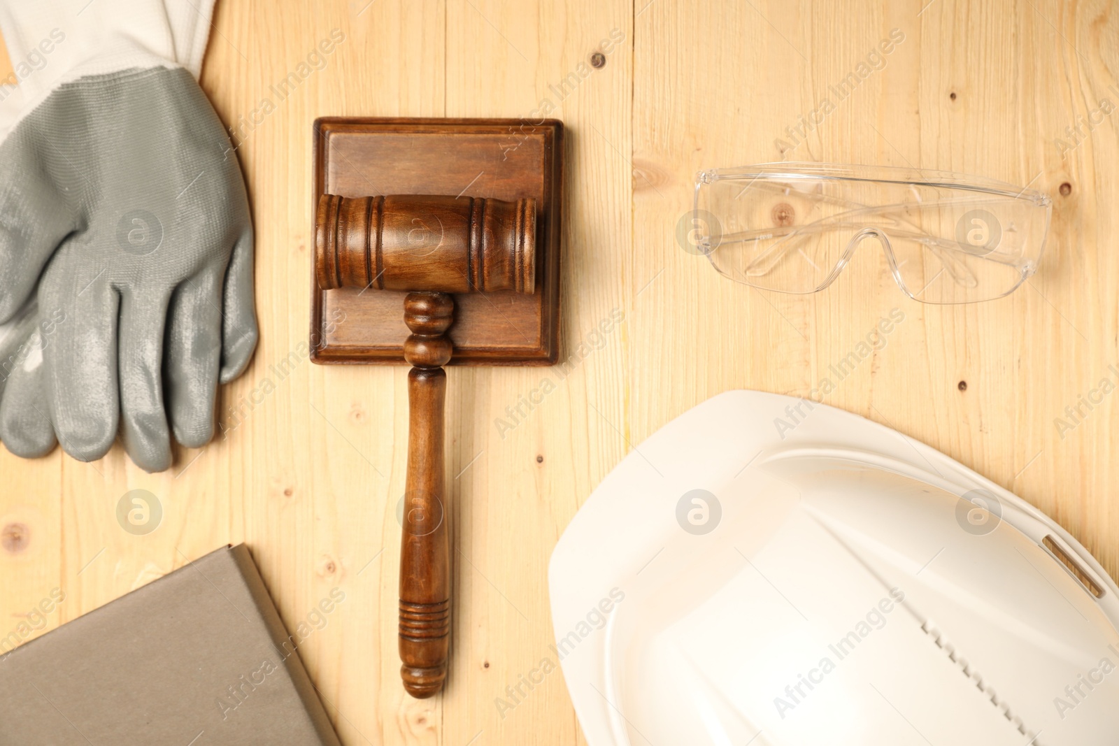 Photo of Accident at work concept. Gavel, book and protective gear on wooden table, flat lay