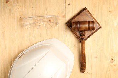 Photo of Accident at work concept. Gavel, hardhat and protective goggles on wooden table, flat lay