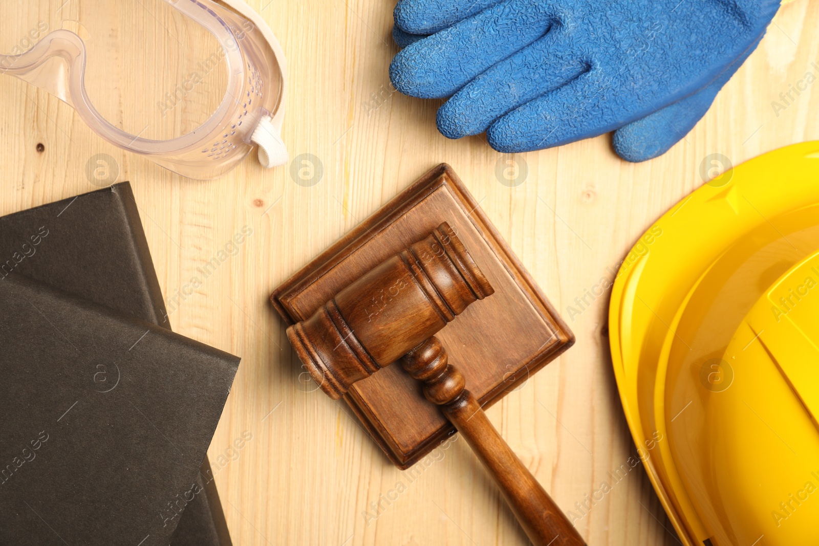 Photo of Accident at work concept. Gavel, books and protective gear on wooden table, flat lay