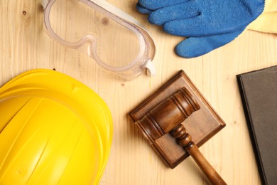 Photo of Accident at work concept. Gavel, book and protective gear on wooden table, flat lay