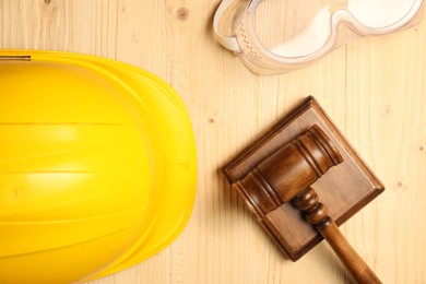 Photo of Accident at work concept. Gavel, hardhat and protective goggles on wooden table, flat lay