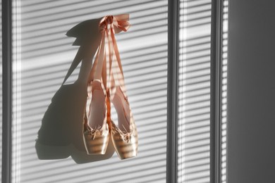 Photo of Pair of beautiful pointe shoes hanging on white wall, space for text