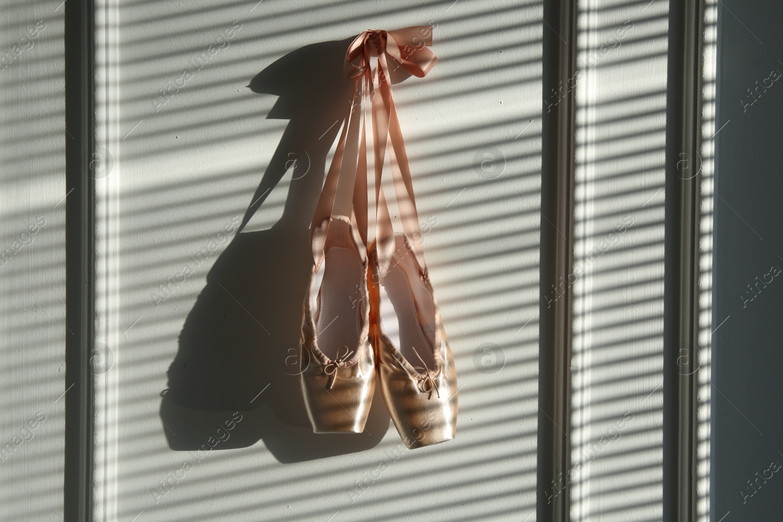 Photo of Pair of beautiful pointe shoes hanging on white wall