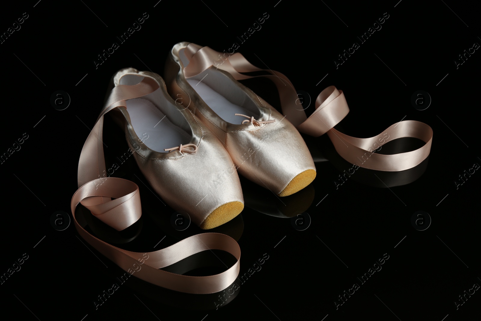 Photo of Pair of beautiful pointe shoes on black mirror surface