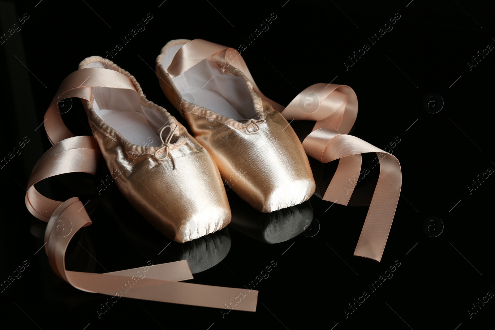 Photo of Pair of beautiful pointe shoes on black mirror surface