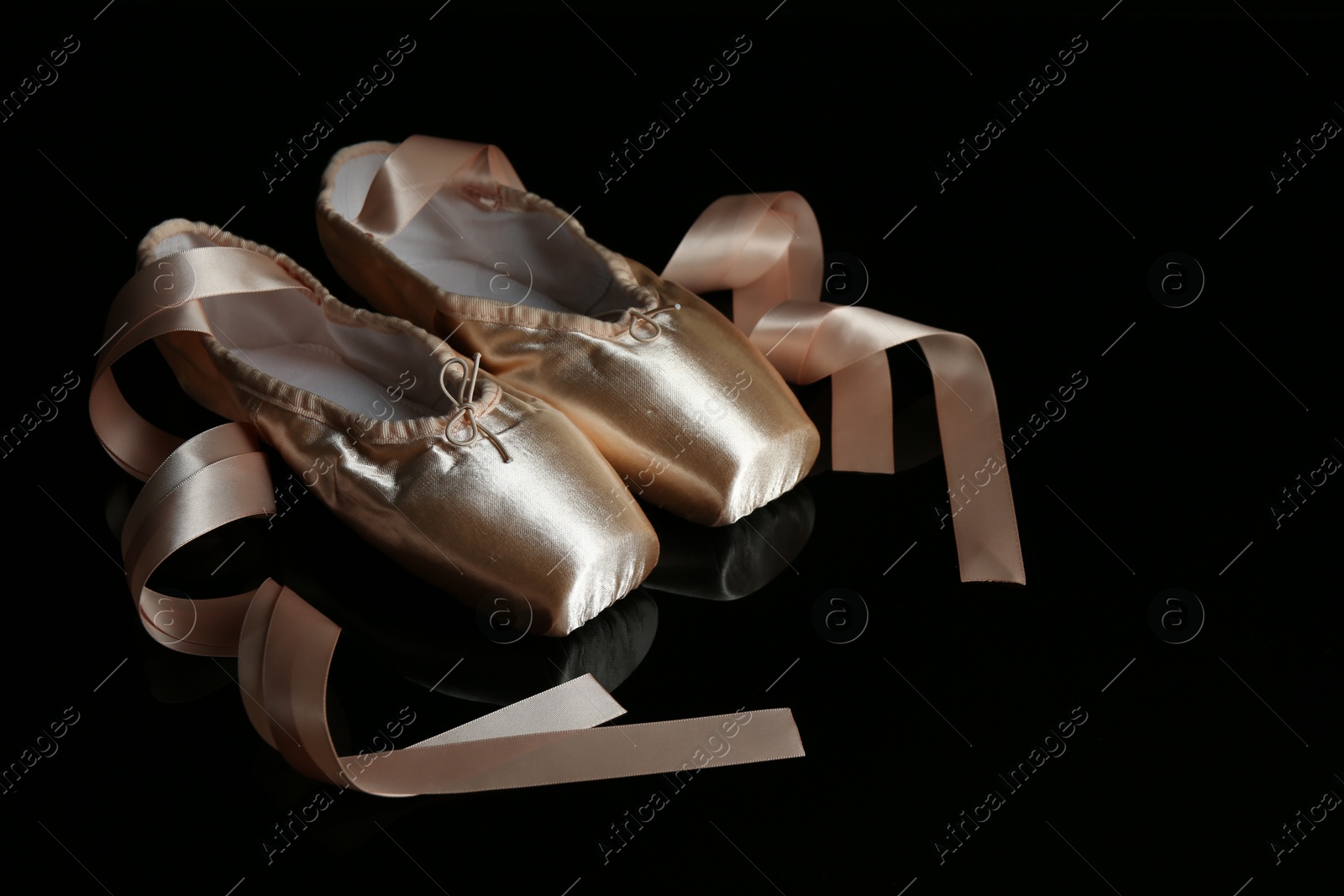 Photo of Pair of beautiful pointe shoes on black mirror surface