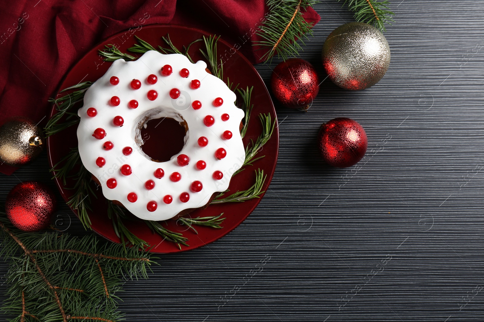 Photo of Tasty Christmas cake with red currants, rosemary, fir and baubles on black wooden table, flat lay. Space for text