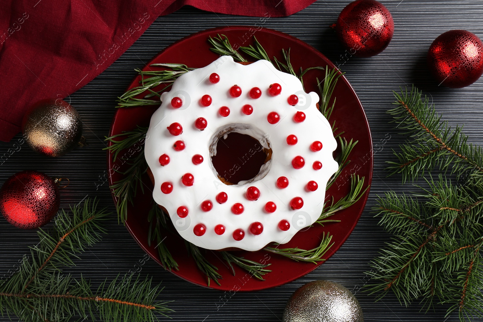 Photo of Tasty Christmas cake with red currants, rosemary, fir branches and baubles on black wooden table, flat lay