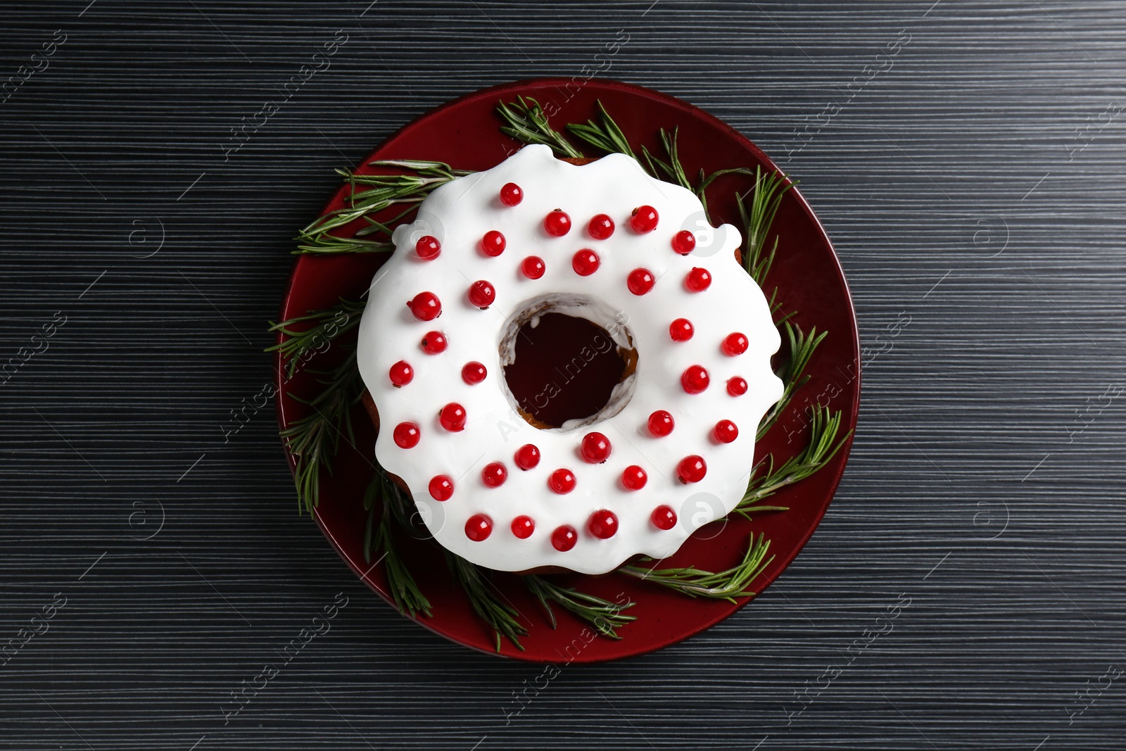 Photo of Tasty Christmas cake with red currants and rosemary on black wooden table, top view