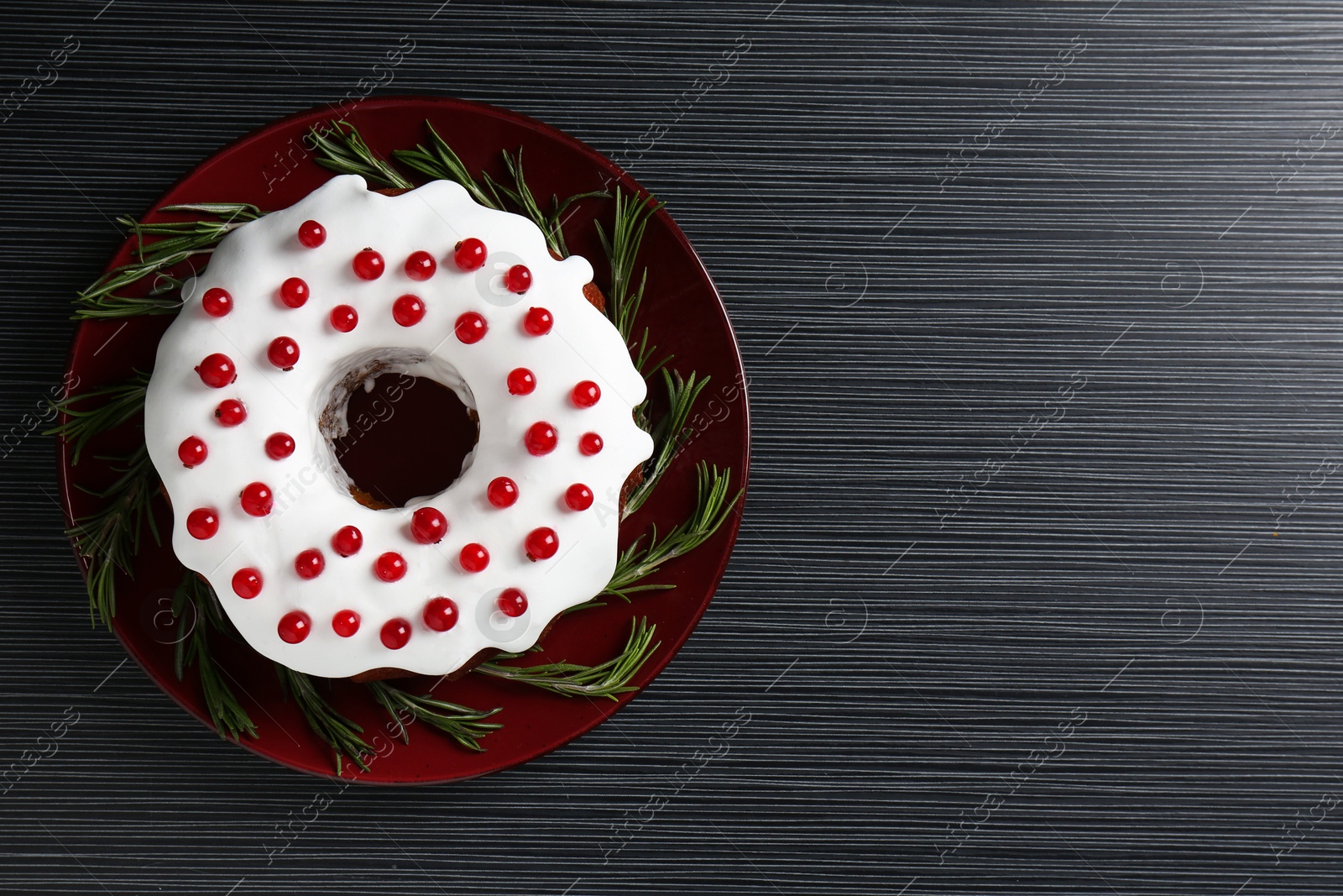 Photo of Tasty Christmas cake with red currants and rosemary on black wooden table, top view. Space for text