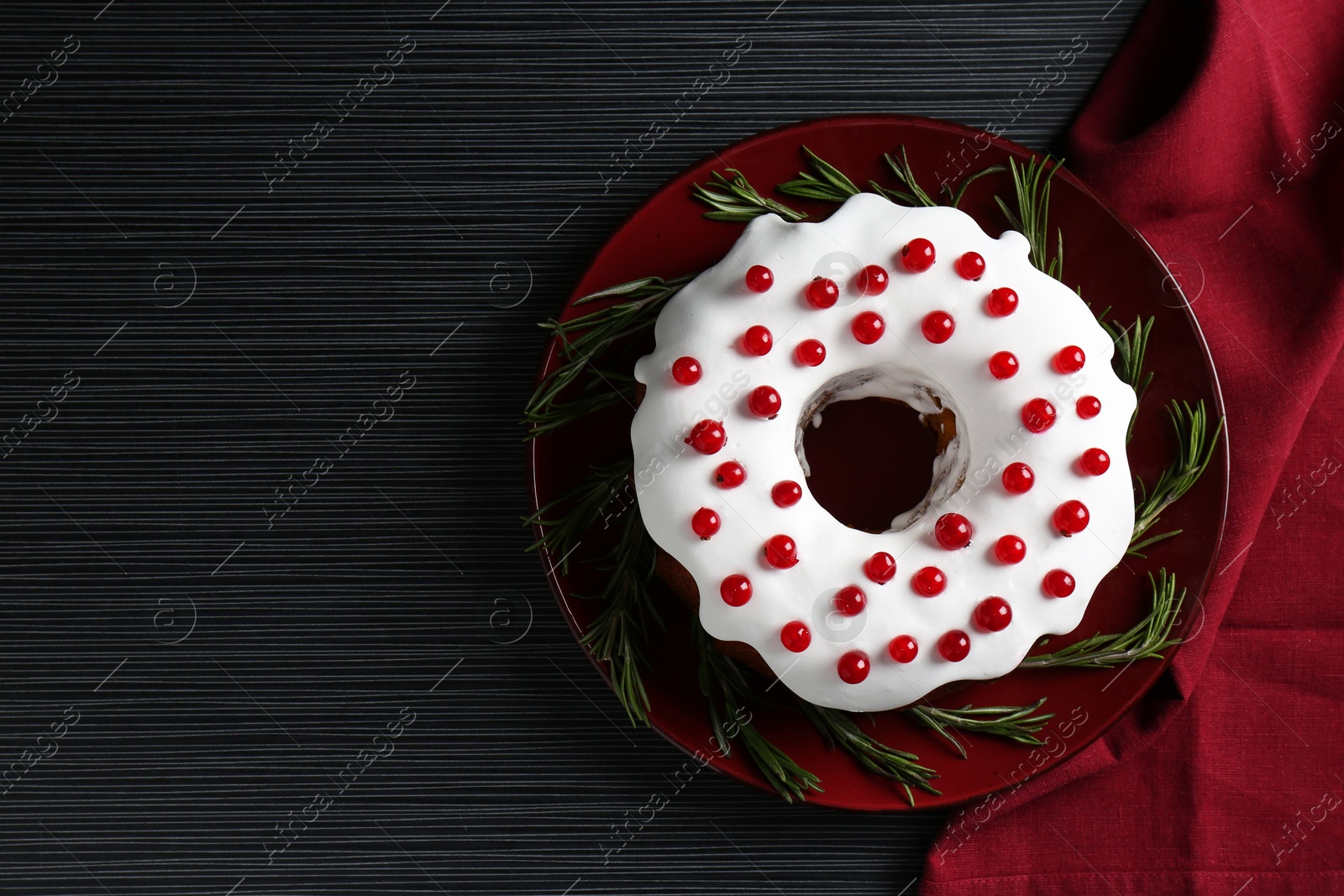 Photo of Tasty Christmas cake with red currants and rosemary on black wooden table, top view. Space for text